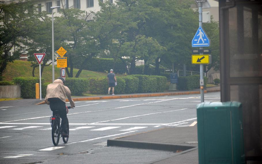 A bicyclist and pedestrian make their way towards the main gate at Yokosuka Naval Bas, Japan, on Aug. 16, 2024, as Typhoon Ampil passed Japan's eastern coast. 