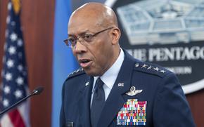 An Air Force officer in blue dress uniform speaks into a microphone in front of U.S. flags and the emblem of the Pentagon.