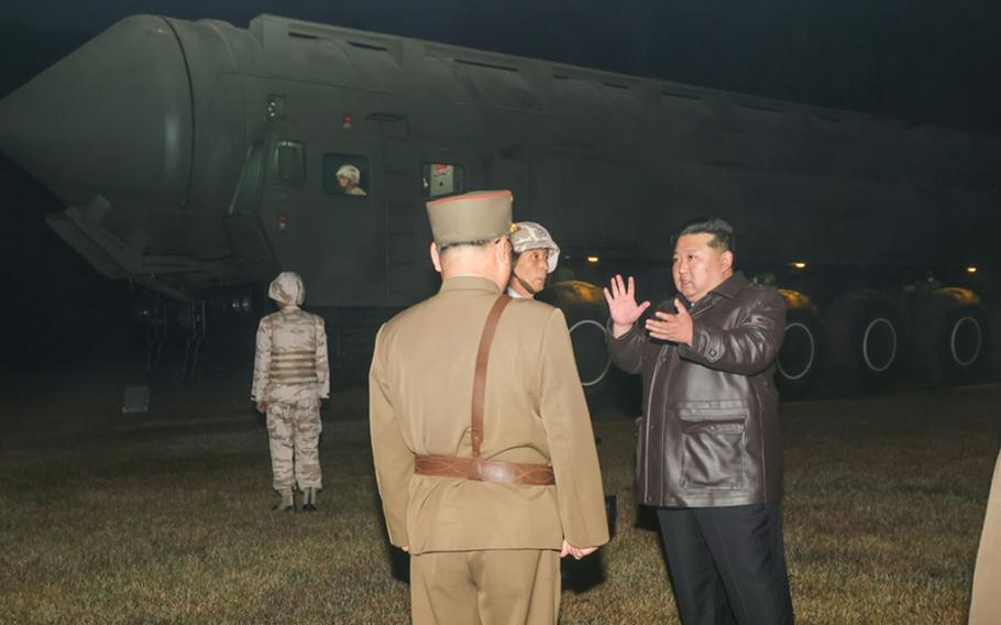 Kim Jong Un speaks with military leaders with an intercontinental ballistic missile in the background.