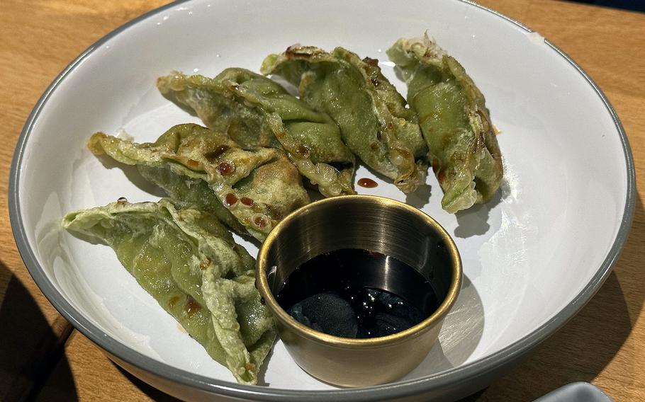 Green gyoza with dipping sauce on a plate.