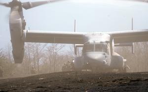 Soldiers walk away from an Osprey on the ground with its propellers rotating.