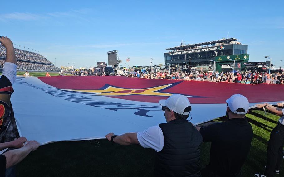 A flag is being unfolded by multiple people on a racetrack