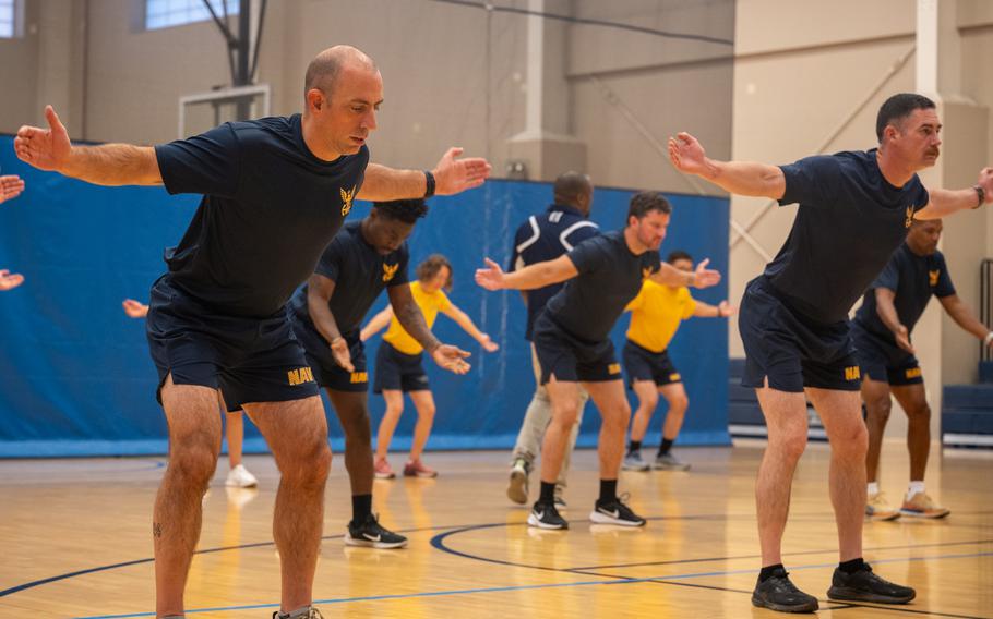 Service members hold their arms out to the sides in a gym during a command fitness leader certification course on Camp Lemonnier.