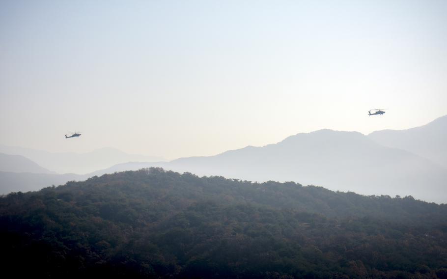 Seen from a distance, Apache helicopters fly over mountains of a live fire complex.