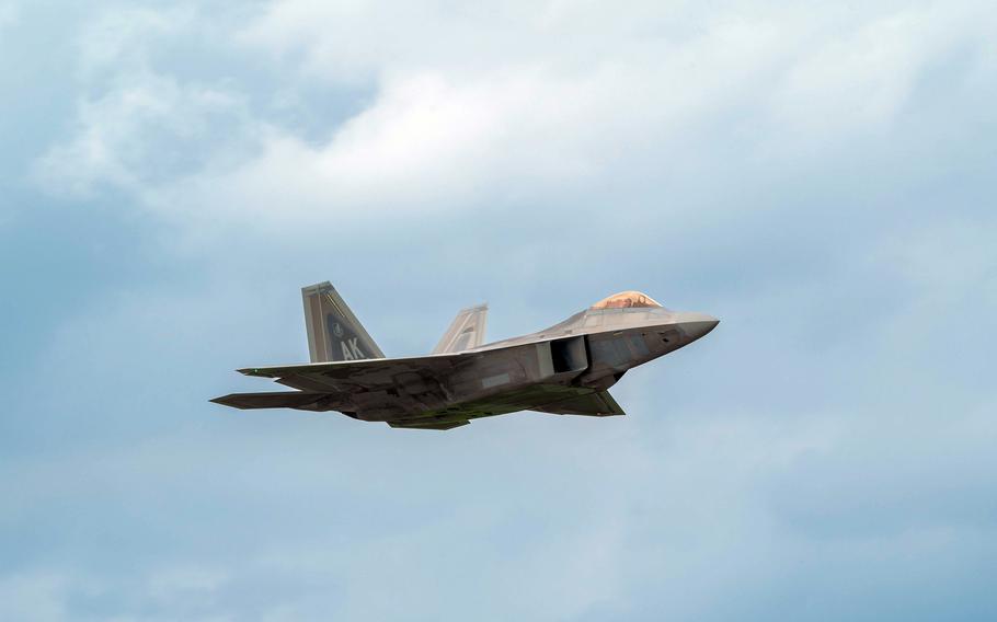 The F-22A Raptor flies with a cloudy sky in the background.