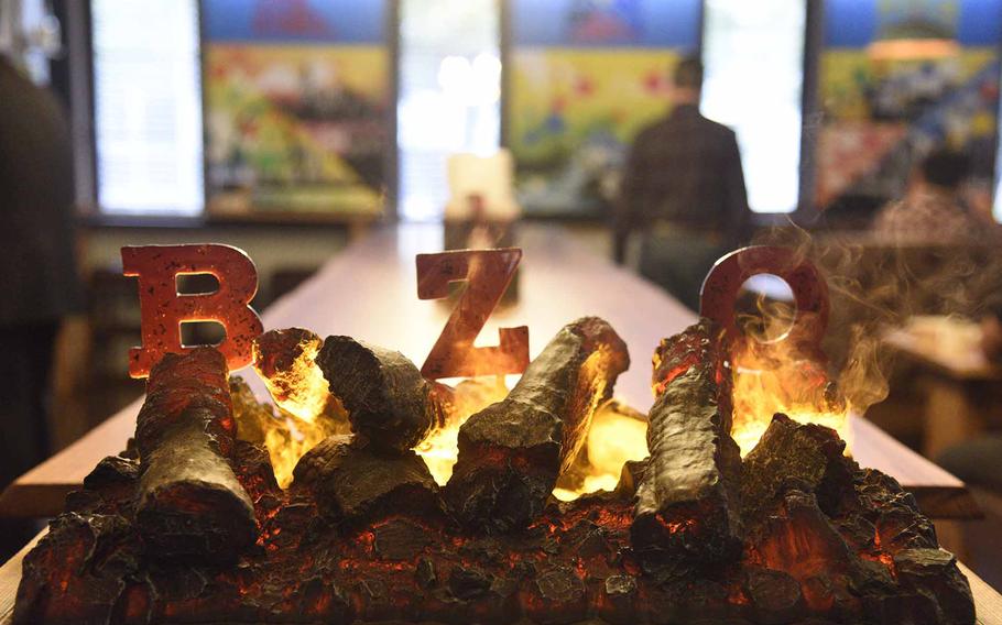 An artful display of letters and burning logs sits in the foreground; a long restaurant table is in the background.