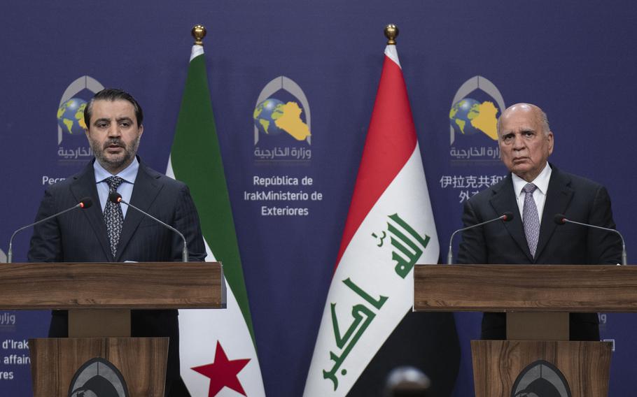 Foreign ministers representing Iraq and Syria stand at podiums with their respective national flags behind them.