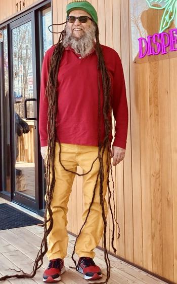 A man is standing up to show that his dreadlocks are much longer than he is tall.