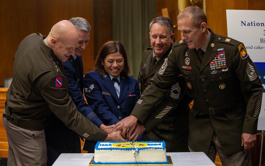 Five high-ranking members of the U.S. military all place their hands on a knife cutting a cake.