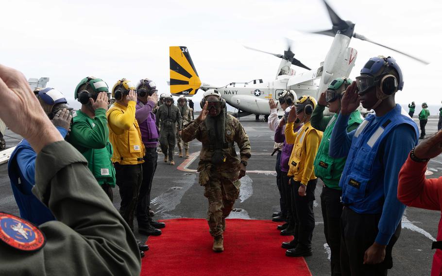 A U.S. Army general walks on a red carpet as a line of sailors salutes him aboard the USS Carl Vinson.