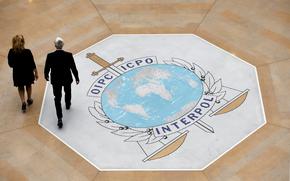 FILE - People walk on the Interpol logo at the international police agency headquarters in Lyon, France, on Nov. 8, 2018. (AP Photo/Laurent Cipriani, File)