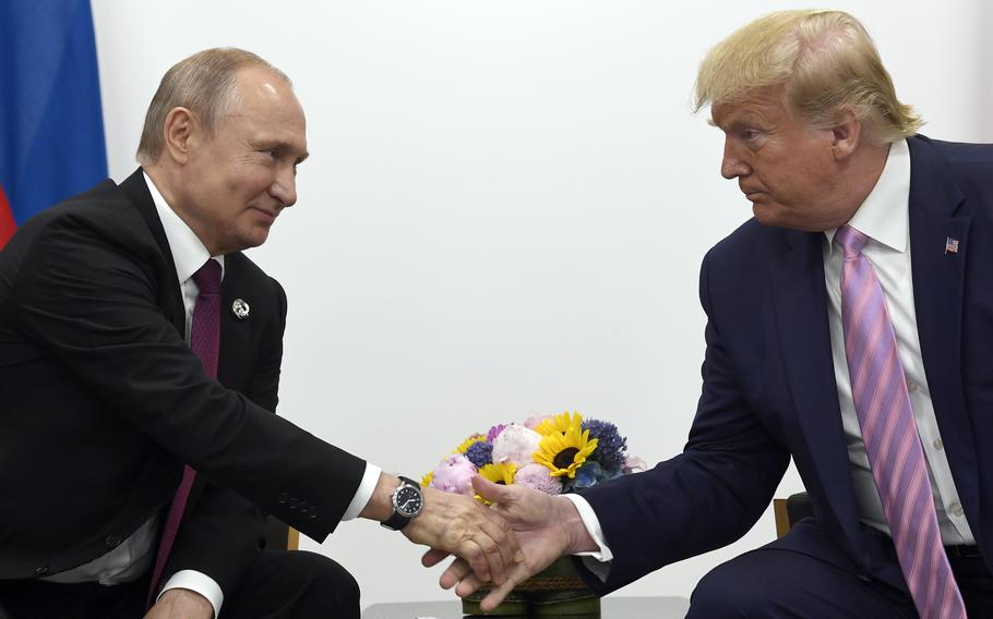 Donald Trump and Vladimir Putin shake hands in front of a vase of flowers while seated.