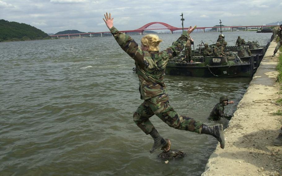 A female soldier jumps into a river with her arms outstretched into the air.