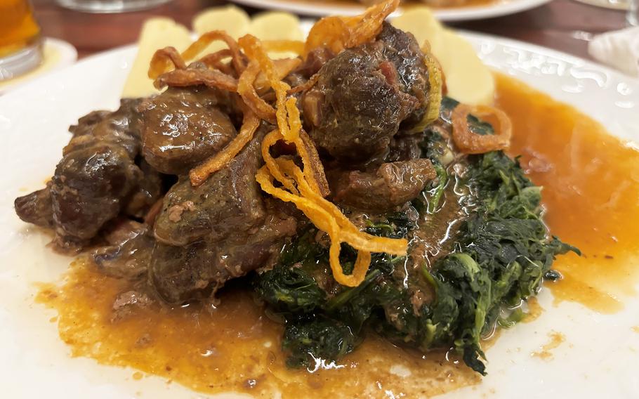 The roasted wild boar loin with fried onions atop a bed of sauteed spinach at Purkmistr in Pilsen, Czech Republic. It is served with potato dumplings. 