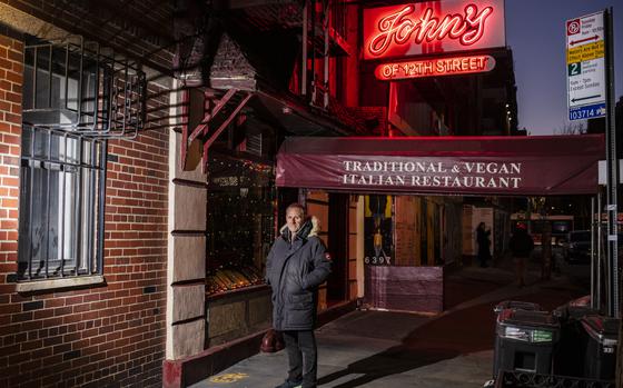 A man stands in front of John’s of 12 Street in New York. 