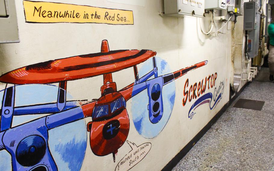 A mural in a hallway of the USS Dwight D. Eisenhower shows a C-2 Hawkeye surveillance aircraft. Referring to the Houthi attacks, the image reads: 