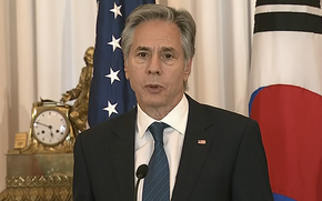 Antony Blinken speaks into a microphone while standing in front of U.S. and South Korean flags.