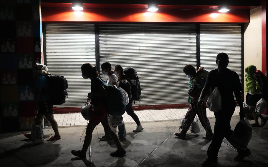 A group of migrants, shown in shadows, walk past.