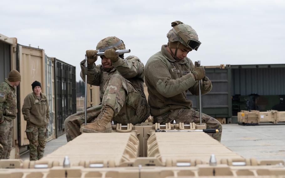 Soliders, working back to back, prepare missiles for shipping.