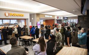 People stand in line in front of a Popeyes, Burger King, Pizza Hut and Taco Bell in a food court.