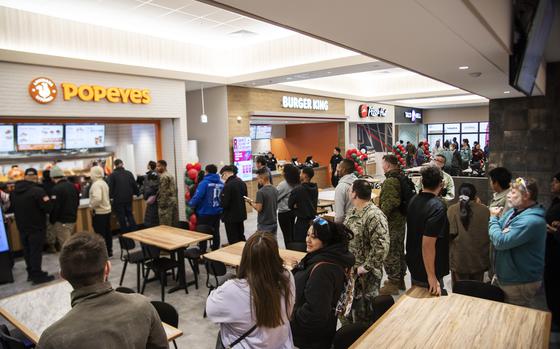 People stand in line in front of a Popeyes, Burger King, Pizza Hut and Taco Bell in a food court.