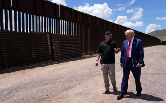 Donald Trump walks with another man along a border wall.