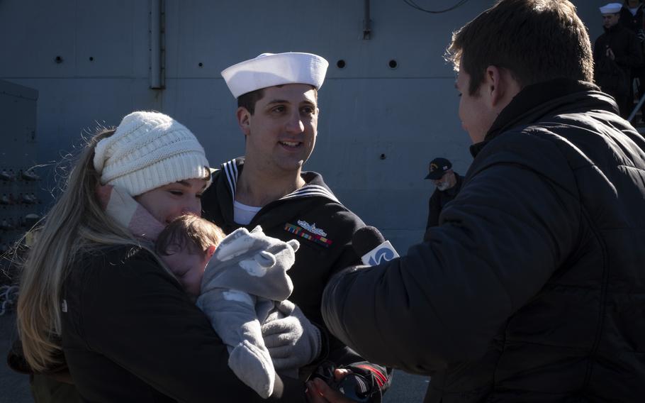 A sailor with his wife and sleeping child answers questions.