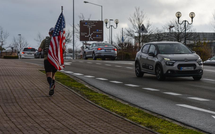 Air Force Master Sgt. Trevor Derr, flight chief, 721st Aircraft Maintenance Squadron, runs in body armor and with American flag near the base exchange at Ramstein Air Base, Germany, Dec. 7, 2021. Derr has been spotted at Air Force bases around the world while he runs in honor of his friend, Tech. Sgt. Daniel Swaney, whom he lost to suicide.