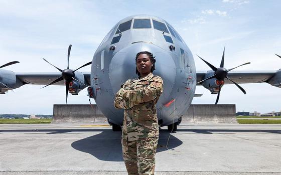 A woman in uniform with her arms crossed stands in front of a plane.