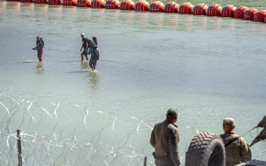 Texas Department of Public Safety (DPS) highway patrol troopers look over the Rio Grande as migrants walk by a string of buoys placed on the water along the Rio Grande border with Mexico in Eagle Pass, Texas, on July 15, 2023, to prevent illegal immigration entry to the US. The buoy installation is part of an operation Texas is pursuing to secure its borders, but activists and some legislators say Governor Greg Abbott is exceeding his authority.