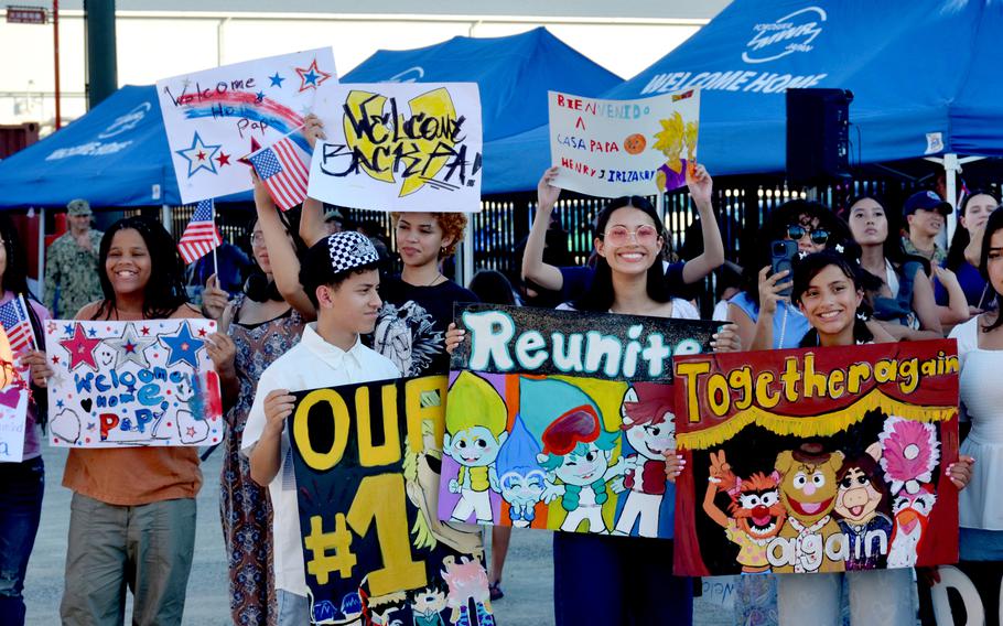 Friends and family hold up signs at Yokosuka Naval Base, Japan, as the USS Blue Ridge eturns home from a 77-day deployment, Tuesday, Aug. 20, 2024. 