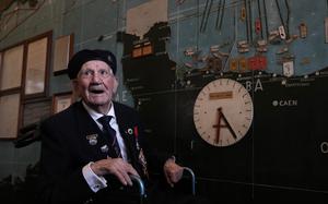 A man in uniform stands in front of a diagram of the D-Day invasion.