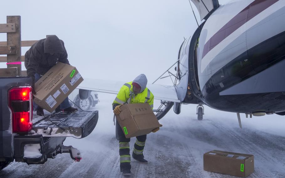 Two men unload packages from a small plane in blizzard conditions.