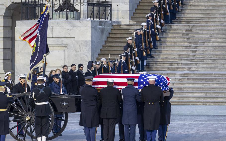 Members of the armed forces carry the flag-draped casket of Jimmy Carter. Others line the steps to the Capitol.