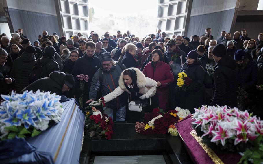 Two caskets, one dressed in light blue and the other in pink, are seen on the left and right corners of the image while mourners in front of the caskets take up most of the rest of the space.