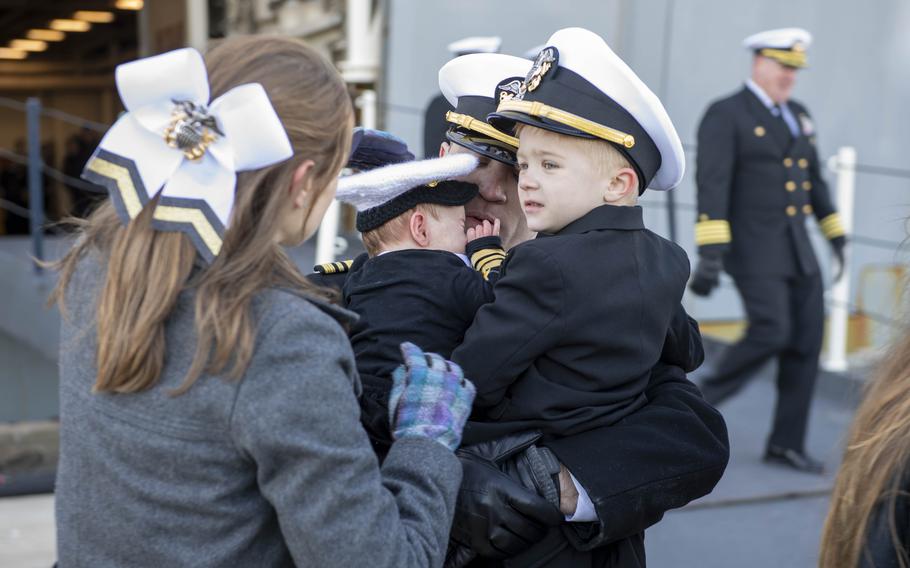 A sailor embraces his two children, both wearing Navy caps and coats. 