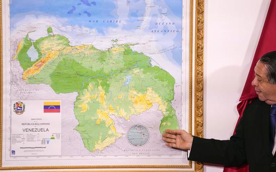 FILE - Chairman of the Special Commission for the Defense of Guyana Essequibo Hermann Escarra, stands next to Venezuela's new map that includes the Essequibo territory, a swath of land that is administered and controlled by Guyana but claimed by Venezuela, during an unveiling ceremony in Caracas, Venezuela, Dec. 8, 2023. (AP Photo/Matias Delacroix, File)