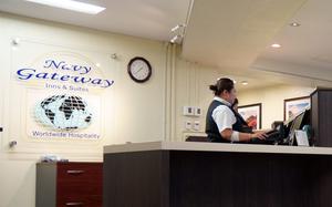 A sign reads Navy Gateway Inns & Suites Worldwide Hospitality as two women work at the front desk of the Yokosuka Naval Base location.