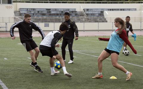 Photo Of A Japanese soccer coach watches American high school players conduct practice drills on a field.