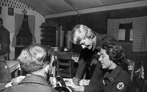 Camp Kaiser, South Korea, December 1958: Lynne Kaelber (seated) and Didi Hasson (standing) chat with two of the men of the 7th Military Police Company at Camp Kaiser. The two women are American Red Cross workers who travel around South Korea to deliver coffee, donuts and some human interaction to American and allied troops stationed in Korea. 

Colloquially known as the "Donut Dollies," the American Red Cross started - at the request of the U.S. government - refreshments at railroad junctions for military on troop trains. By the end of the war, the Red Cross operated some 700 fixed canteens, many operated by several of the 55,000 women Red Cross volunteers. 
The service again mobilized in World War II, creating clubmobiles  using single decker English Green Line buses, outfitting them with coffee and donut machines and a lounge in the back. Staffed by three American Red Cross volunteers, their aim was to bring a taste of home to the front lines. 

The service was resurrected again during the Korean War, during which some sources say they earned their enduring nickname, but became most visible during the Vietnam War when between 1962 and 1973 the "Dollies" logged over 2 million miles by jeep, deuce-and-a-half, and helicopter, but - according to the Army Historical Foundation - did not pass out a single donut. Instead they brought smiles, songs, games and as always, a touch of home to the guys in country.

Read how the troops reacted to the "Dollies" in 1958 and check out additional photos here. 

META TAGS: South Korea; American Red Cross; Donut Dollies; U.S. Army; U.S. Air Force; morale; military life; women in the military; 7th Military Police Company; volunteer