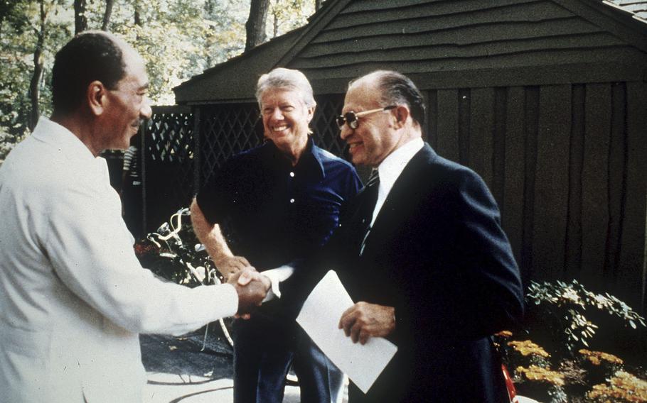 Anwar Sadat shakes hands with Menachem Begin as Jimmy Carter looks on.