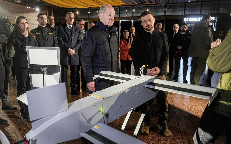 The leaders of Ukraine and Germany stand before a drone in a room.