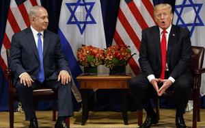 Donald Trump and Benjamin Netanyahu sit next to each other in chairs in front of U.S. and Israeli flags.