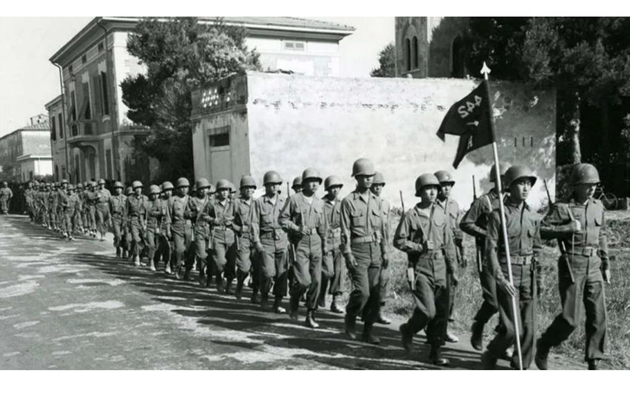 Army soldiers march through town carrying a flag from the 442nd Regiment.