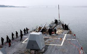 Sailors, seen from above and behind, man the rails on a U.S. Navy destroyer as it travels down a river.