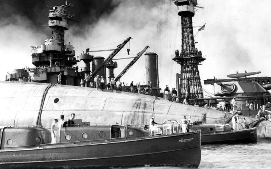 A black-and-white 1940s-era image of a ship upside down in the water, with rescue workers standing on the hull and support boats next to it in the foreground.