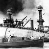 A black-and-white 1940s-era image of a ship upside down in the water, with rescue workers standing on the hull and support boats next to it in the foreground.