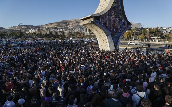 A large group of protesters gather in a public square next to a monument.