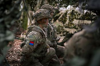 A U.K. soldier wearing camouflage and face paint sits with her squad.