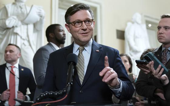 House Speaker Mike Johnson gestures with his hand while standing at a podium and speaking into a microphone.